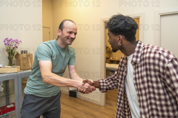 Two men from different backgrounds smiling and shaking hands in an office, symbolizing friendly
