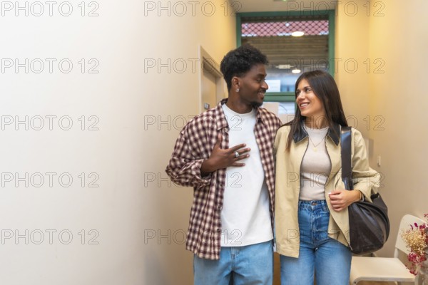Young intercultural couple walking indoors, smiling and looking at each other with joy and