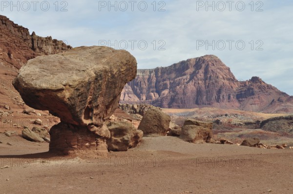 A gigantic rock sits on red desert sand in front of a barren rocky landscape, Grand Canyon National