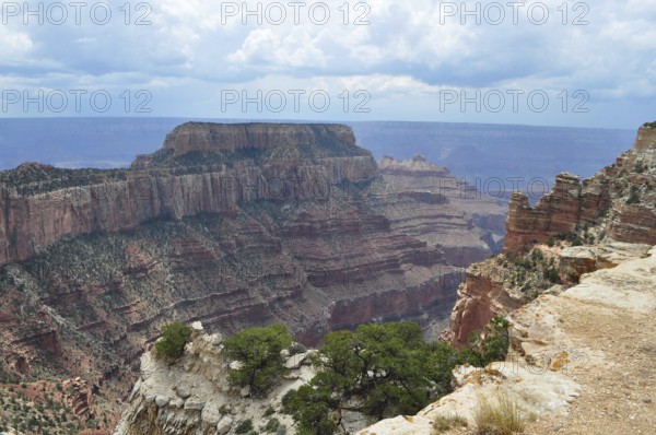 Extensive view of a canyon with deep valleys and steeply sloping cliffs under a cloudy sky, Grand