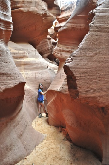 Girls in a narrow part of a sandstone canyon surrounded by bright orange rock walls, Antelope