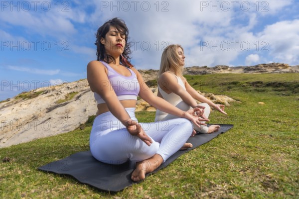 Two young women meditating on yoga mats outdoors, finding peace and mindfulness in nature,