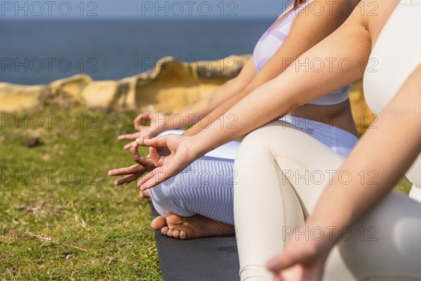 Women practicing meditation outdoors, sitting in a mudra position on yoga mats on a green