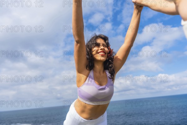 Woman standing on a cliff in sporty wear, arms raised in a joyful yoga stretch, eyes closed,