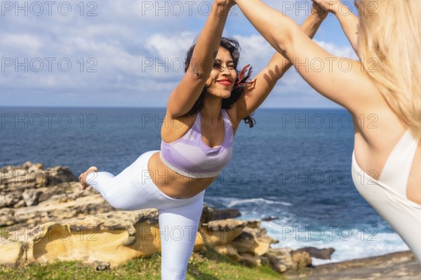 Two women practicing an acrobatic partner yoga pose on a cliff overlooking the ocean, focusing on
