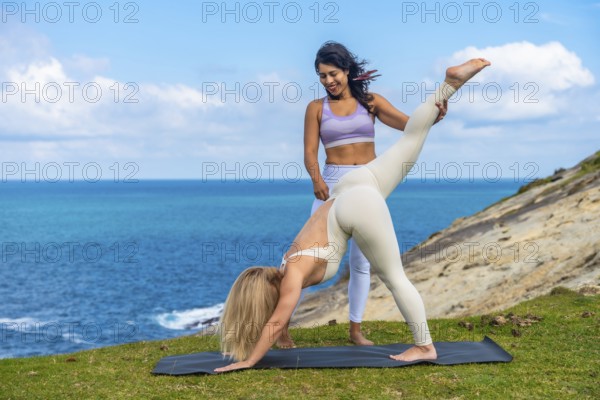 Two women stretching on a yoga mat during an outdoor yoga class by the beautiful blue ocean,