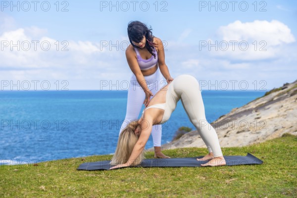 Two women practicing yoga posture with an instructor providing guidance outdoors on a mat, focusing