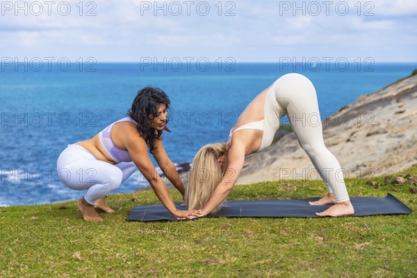 Two women practicing yoga with an instructor correcting posture during a wellness session outdoors