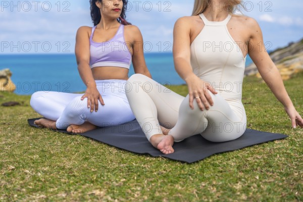 Two diverse women in seated spinal twist yoga poses on mats, meditating and connecting with nature
