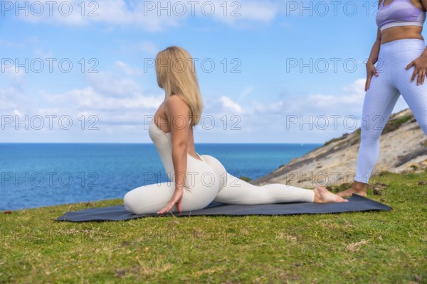 Woman practicing pigeon yoga pose on a mat at an ocean cliff, embracing outdoor wellness and