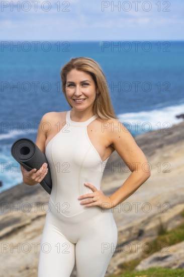 Woman smiling, looking at camera, holding yoga mat, ready for a yoga or meditation session