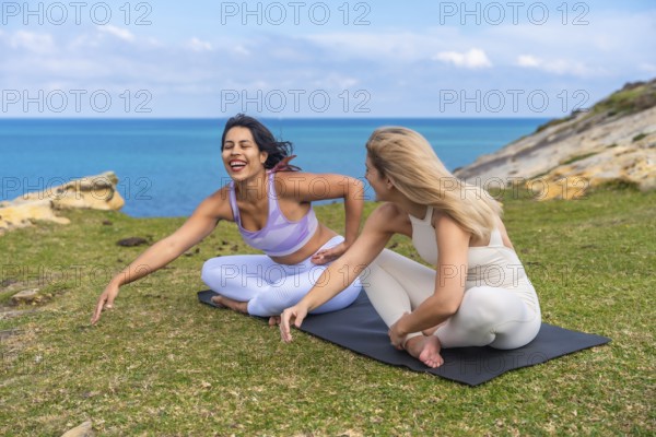 Two happy friends enjoying a yoga session and laughing together on a grassy cliffside overlooking