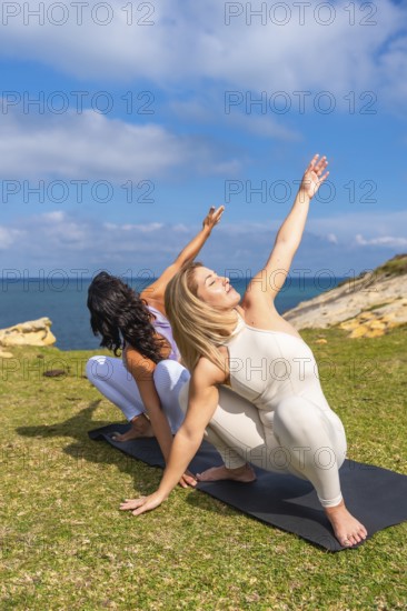 Two women practicing yoga on mats by a calm ocean, stretching into upward poses and finding