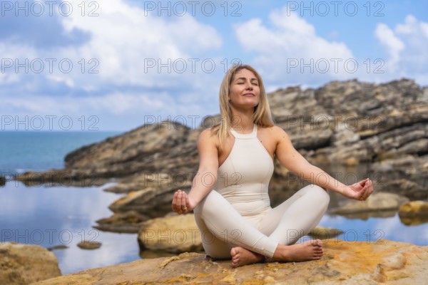 Woman in yoga pose on rocky coastline by the sea, practicing mindfulness and breathing for calm,