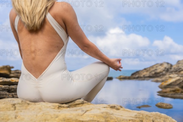 Woman practicing yoga and meditation in a peaceful outdoor setting, sitting in lotus pose on rocks