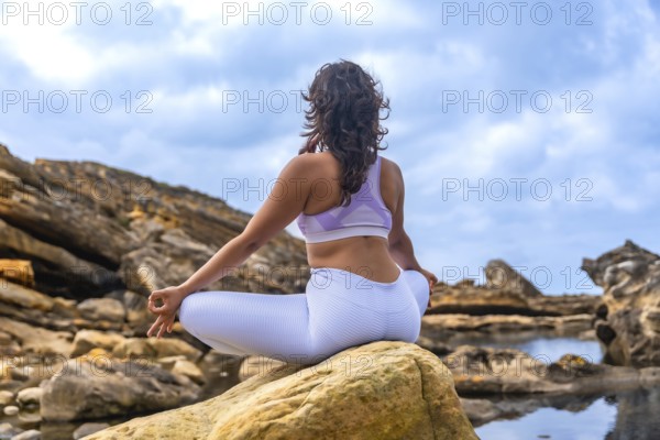 Woman sitting in a yoga lotus position on a rock, practicing meditation and mindfulness in a