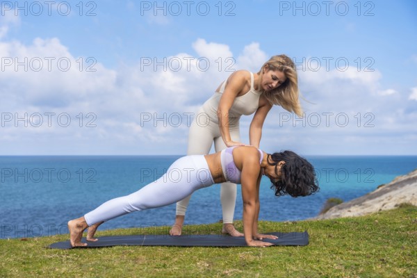 Female yoga instructor assisting a woman in plank pose on a mat, emphasizing proper alignment and