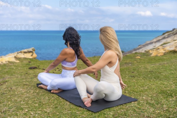 Two diverse women performing a seated spinal twist yoga pose on mats, enjoying a serene outdoor