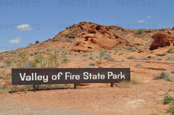 Valley of Fire State Park sign against a red rocky landscape under a blue sky, Valley of Fire State