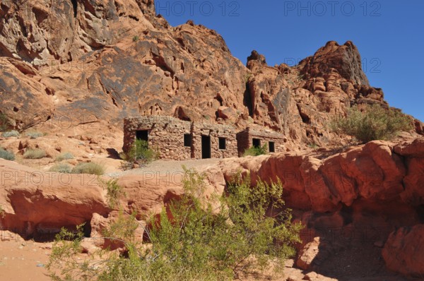 Abandoned stone houses nestled in a red rocky landscape under clear skies, Valley of Fire State
