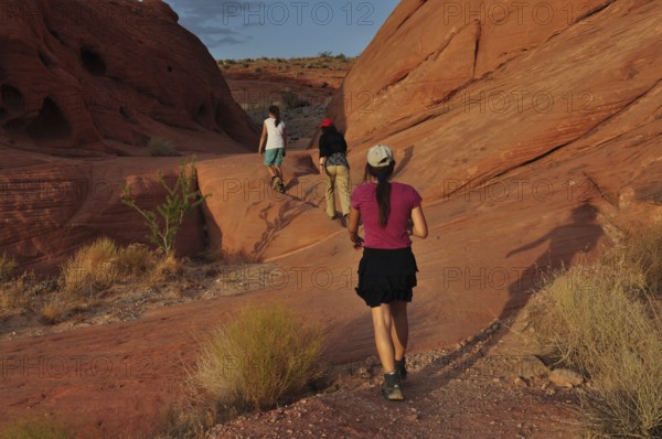 Group of hikers on a trail between red rocks in the desert, Valley of Fire State Park, Nevada, USA