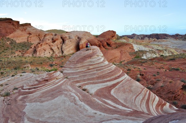 Two people standing on a striped rock formation in a desert landscape, Valley of Fire State Park,