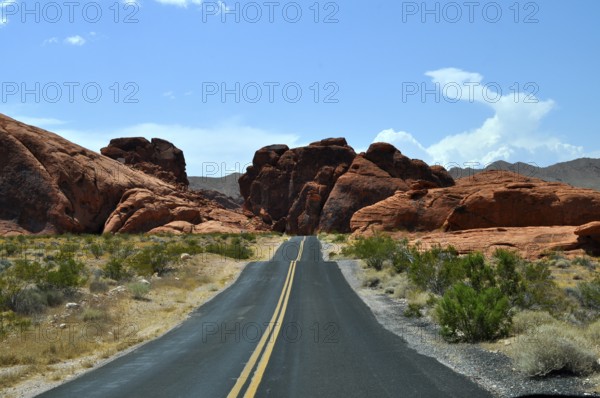 Lonely road leads through red rocky landscape in the desert under blue sky with clouds, Valley of