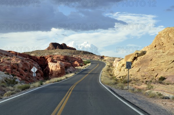 Narrow road with road sign snakes through red rocks under dramatic clouds in the sky, Valley of