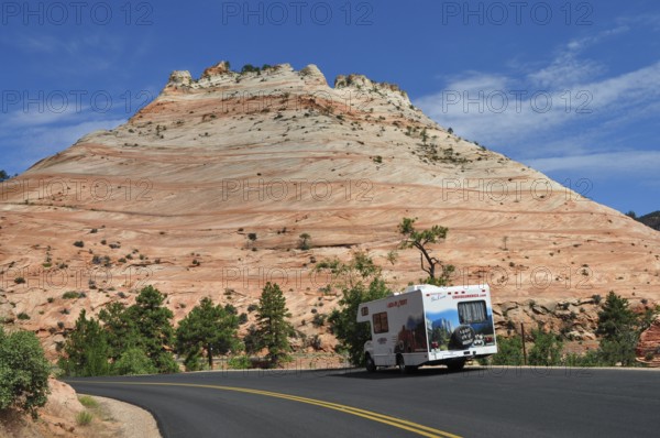 Motorhome drives along a road framed by red rocks and clear skies, Zion National Park, Utah, USA