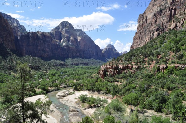 River flows through a lush valley surrounded by imposing mountains and green vegetation, Zion