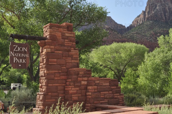 Brick monument with sign in Zion National Park, surrounded by green trees and mountains, Zion