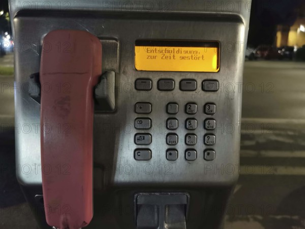 Public telephone at night, display shows error message, sorry currently disturbed, urban area,