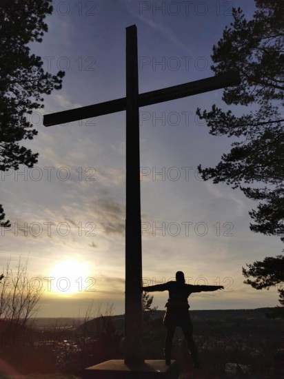 A large cross and a silhouette of a person at sunset, view over Kronach from Kreuzberg, Frankenwald