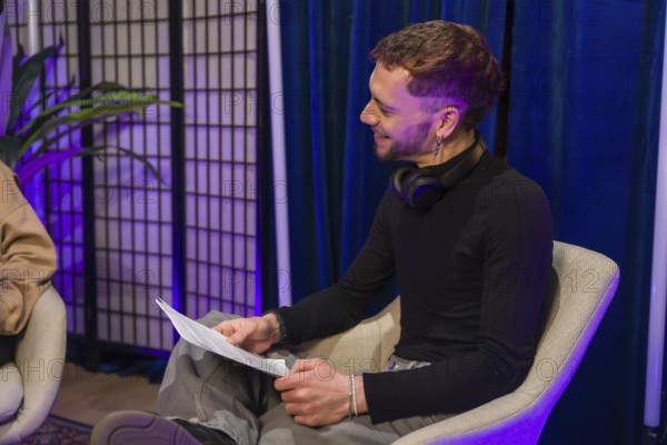 Man in a modern studio setting holding notes and smiling while recording a podcast or creating