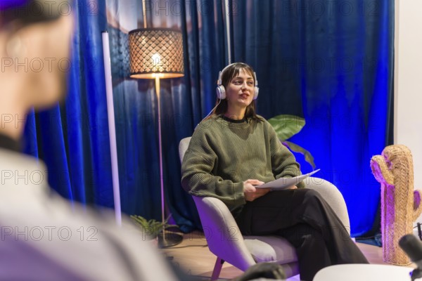 Young woman wearing headphones and holding notes, speaking into a microphone while recording a