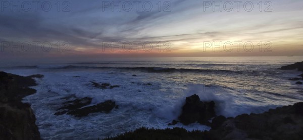 Dramatic sunset with dark clouds and waves, rocks in the foreground, hiking on the Fisherman's