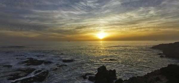 The picture shows an atmospheric sunset over the sea with dramatic clouds, hiking on the