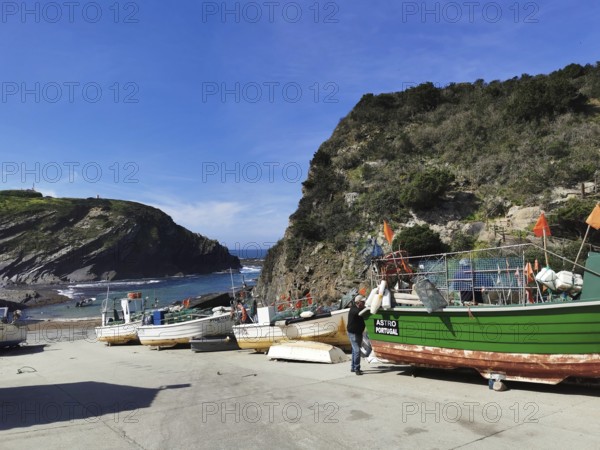 Small harbor with colorful fishing boats against a rocky coastal backdrop, hiking on the