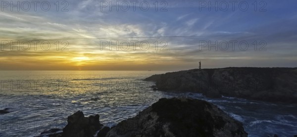 A coastal scene with a lighthouse at sunset. The clouds color the sky colorful, hiking on the