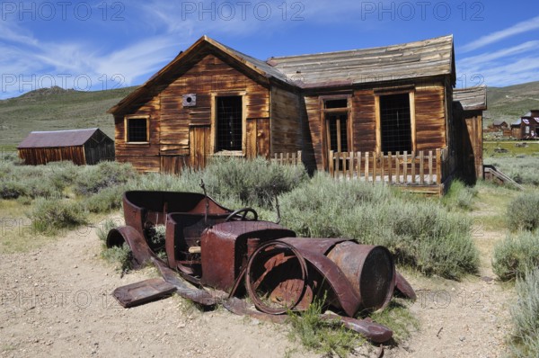 Old wooden house with rusty car wreck in front of it, surrounded by nature, Bodie Ghost Town,