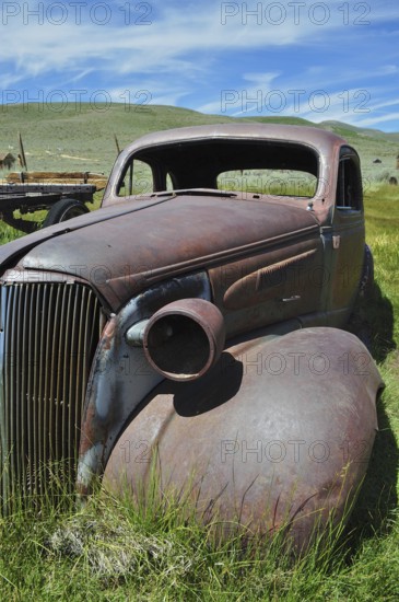 Front view of abandoned rusty car wreck, Chevrolet Coupé, under blue sky, Bodie Ghost Town,