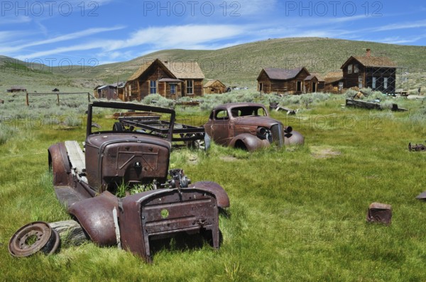 Rusty vehicles, car wrecks, on green area with old abandoned houses, Bodie Ghost Town, California,