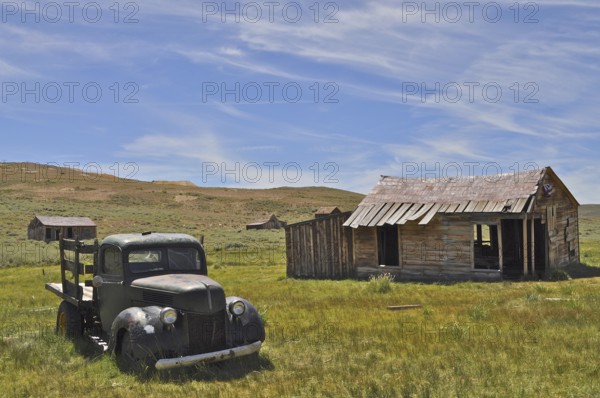 An abandoned car, vintage Ford Model 51 pickup truck, stands next to an old wooden cabin in a