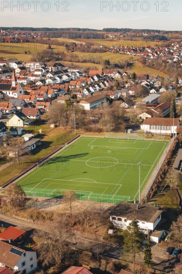 Green sports ground in a village surrounded by houses and hills seen from the air, Wimberg, Calw,