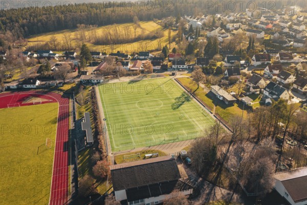 Village with sports field, soccer field and surrounding houses and landscape viewed from the air,