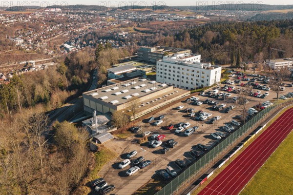 School with parking lot and several cars in a winter landscape with city and hills in the