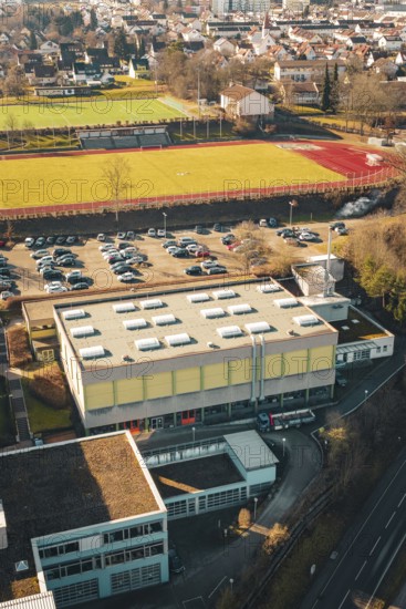 Overview of a sports field with parking lot and school complex in urban and natural surroundings in