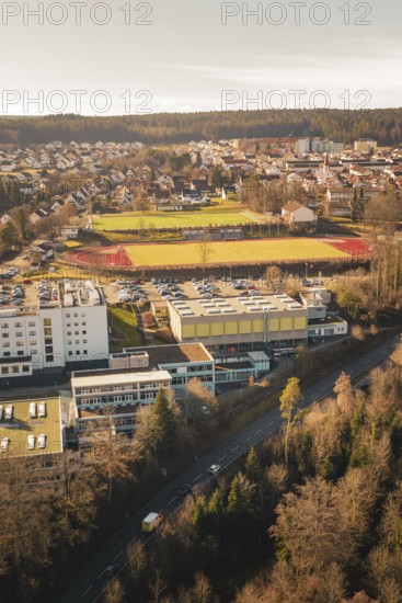 View of a school complex with sports field and playing fields, surrounded by urban landscape and