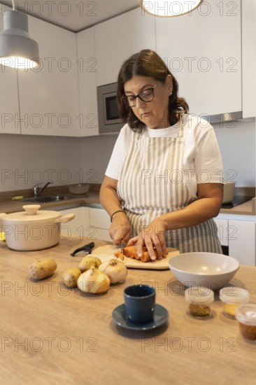Middle aged woman cooking at home, cutting vegetables on wooden countertop. Simple ingredients,