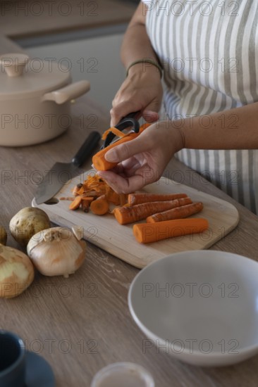 Vertical image of hands peeling carrot in modern kitchen. Casual home cooking, fresh ingredients